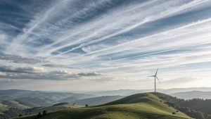 Illustration réaliste d’un paysage avec des nuages superposés, des flux d’air visibles dans le ciel et une éolienne au loin.
