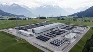 Vue aérienne réaliste d’une installation suisse de stockage d’électricité près de Laufenburg, avec bâtiments techniques, lignes à haute tension et Alpes en arrière-plan.